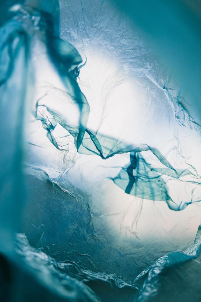 A plastic bag swirls underwater. Light shines through the ripples, making the viewer feel as if they are trapped beneath the surface of the ocean, striving upwards towards a plastic boundary.
