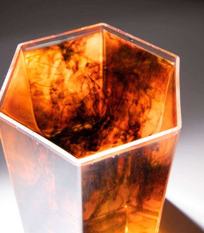 A hexagonal glass contains water that is turning orange due to the presence of some viscous liquid permeates it.